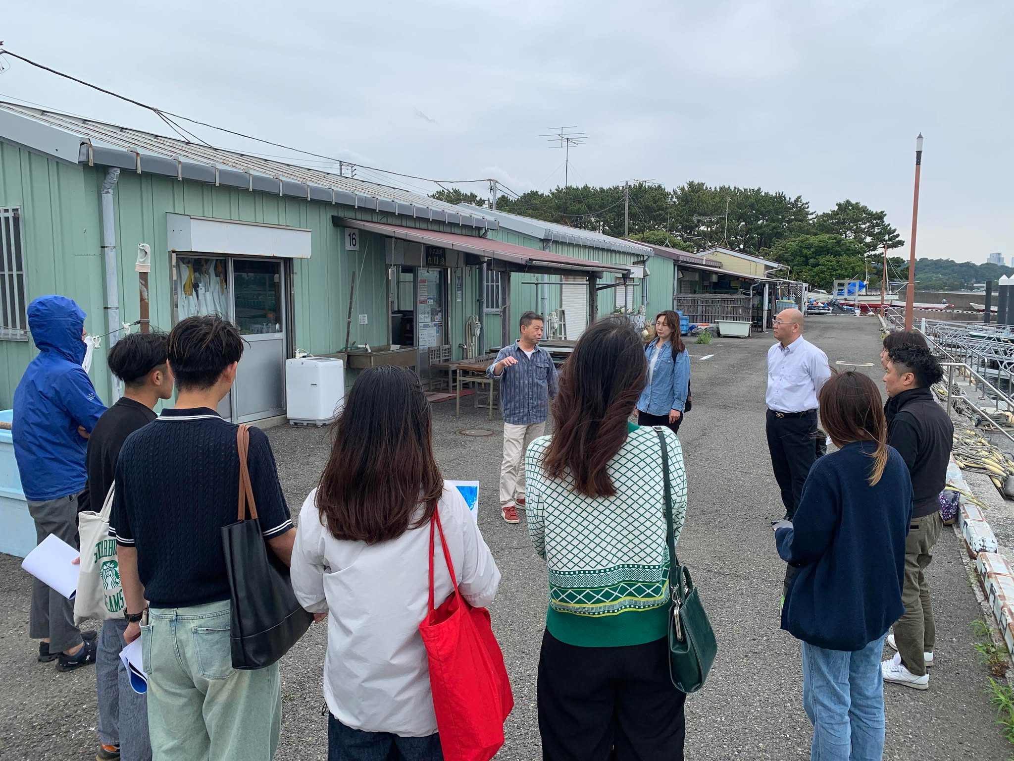 金沢漁港の施設前で海洋環境について説明を受けるTHE FISH開発チームの参加者たち