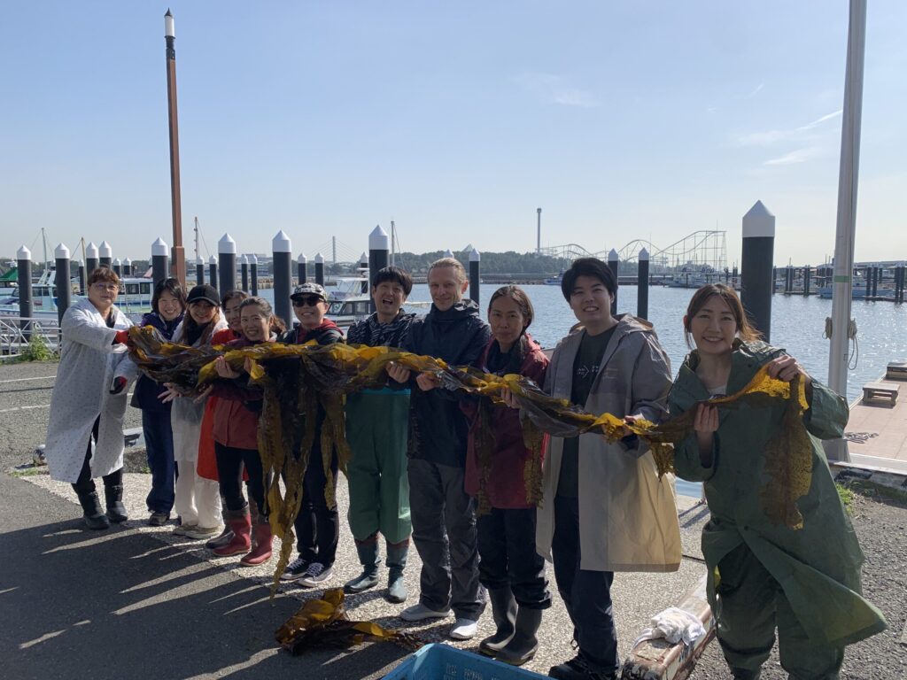 海辺で海藻を広げる作業を行う11人のグループ
