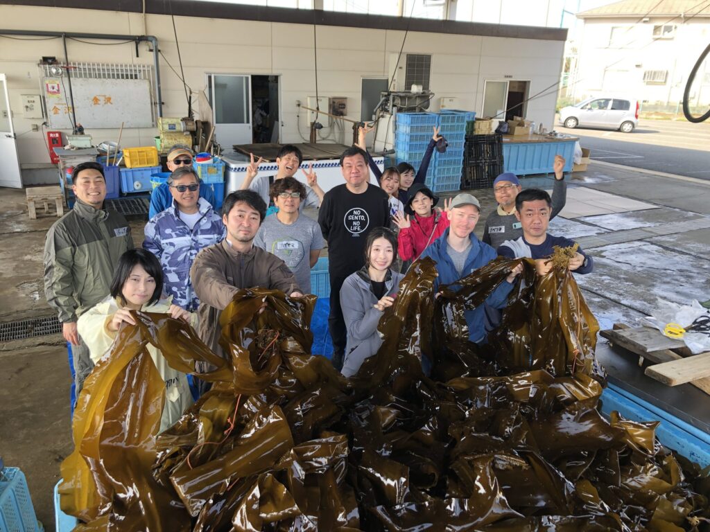 コンブを持ち上げ記念撮影を行う15人のグループ
